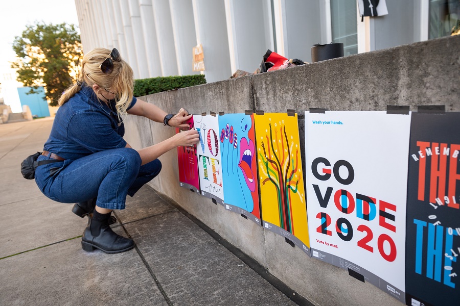CMU Libraries employee taping posters encouraging voting in the 2020 general election to a wall outside of Hunt Library