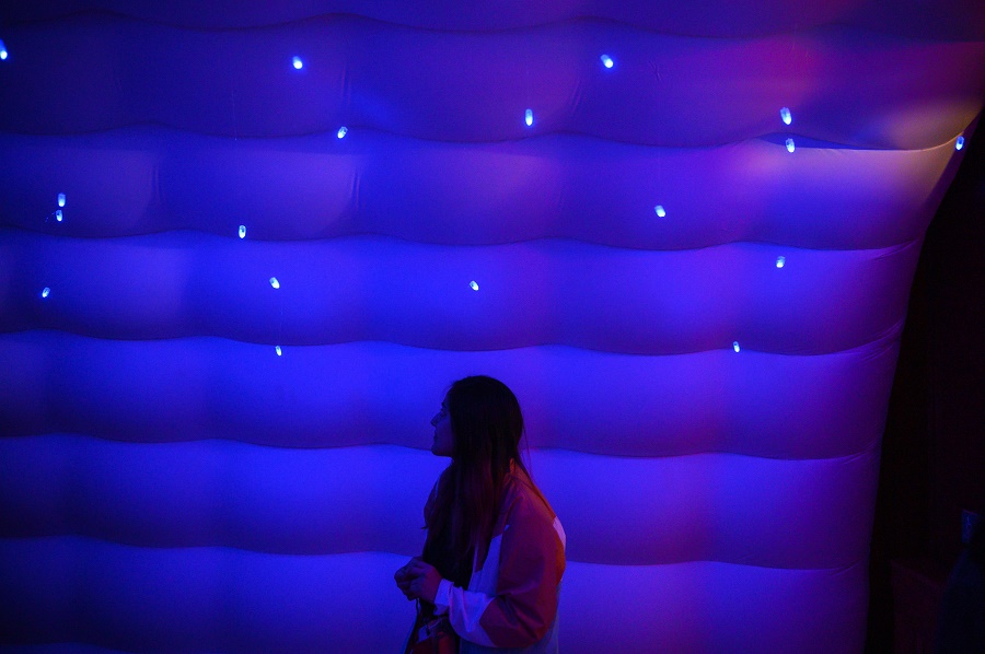 Student in blue-lit inflatable environment looking at twinkle lights above